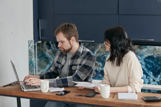 A couple reviews bills and finances at a desk with a laptop and papers. Indoor setting, focused on budgeting. Gaming creators pricing models: how deal structures work