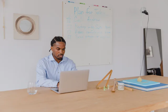 An adult man in a blue shirt working on a laptop in an office with a whiteboard. A one-page strategy framework linking audience need, capacity, income and stop rules
